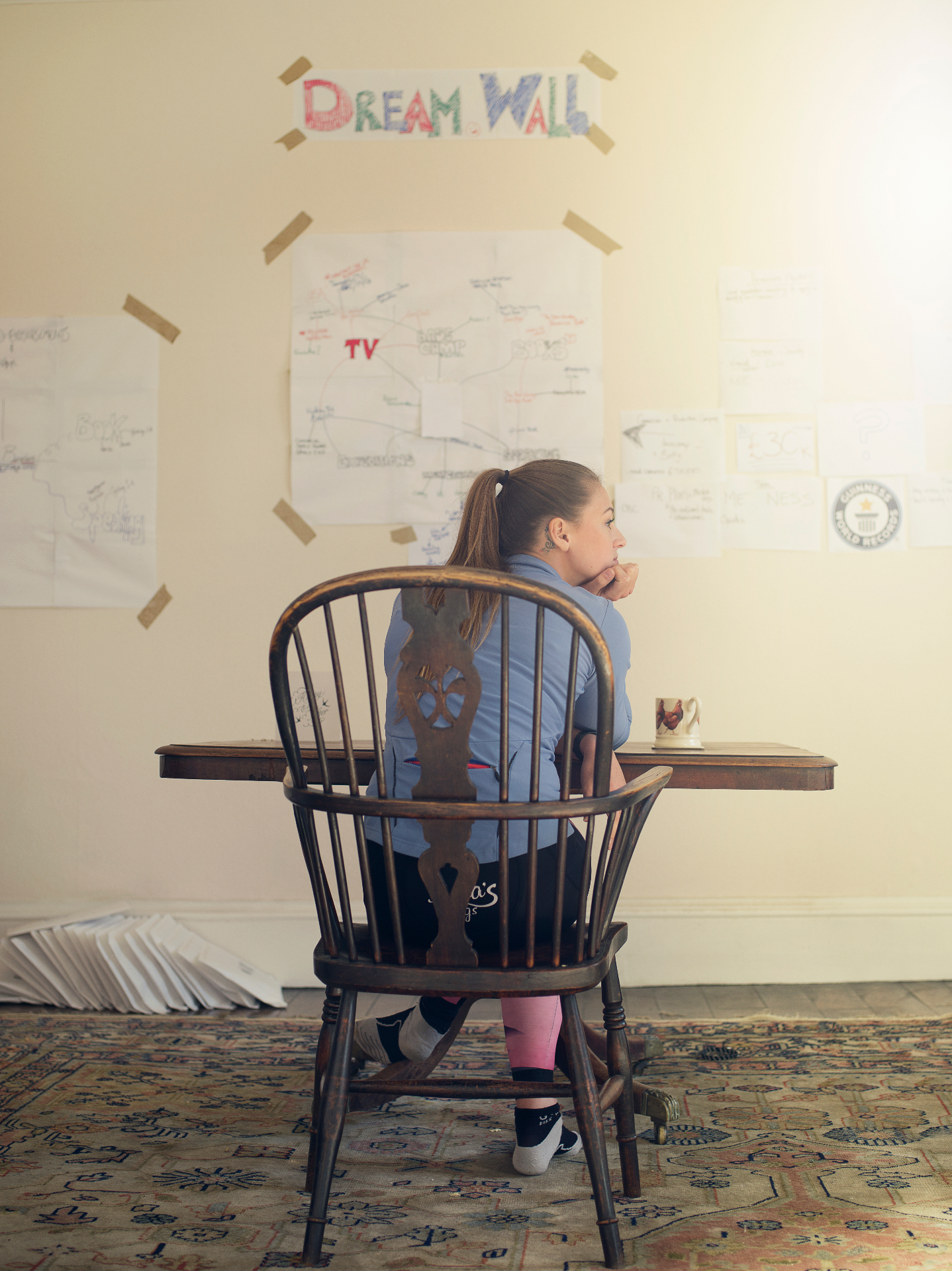 Laura seated at a desk in front of her handwritten dream wall of goals and expedition plans