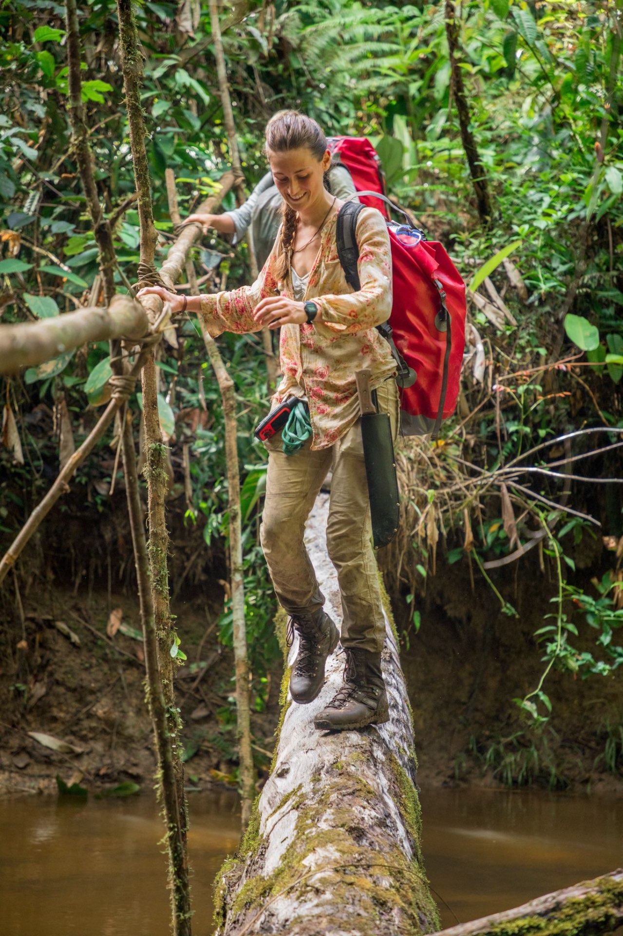 Laura crossing a jungle creek on a fallen log with a pack
